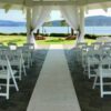 A wedding ceremony with white chairs and a tent.