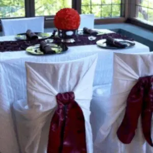 A table with white cloth and red chair covers.