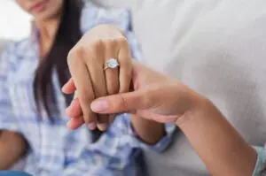 A woman is holding her wedding ring while someone holds it.