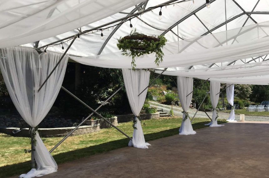 A tent with white curtains and greenery hanging from it.