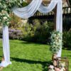 A wedding arch with white draping and flowers.