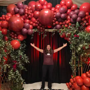 A woman standing in front of an arch made out of balloons.