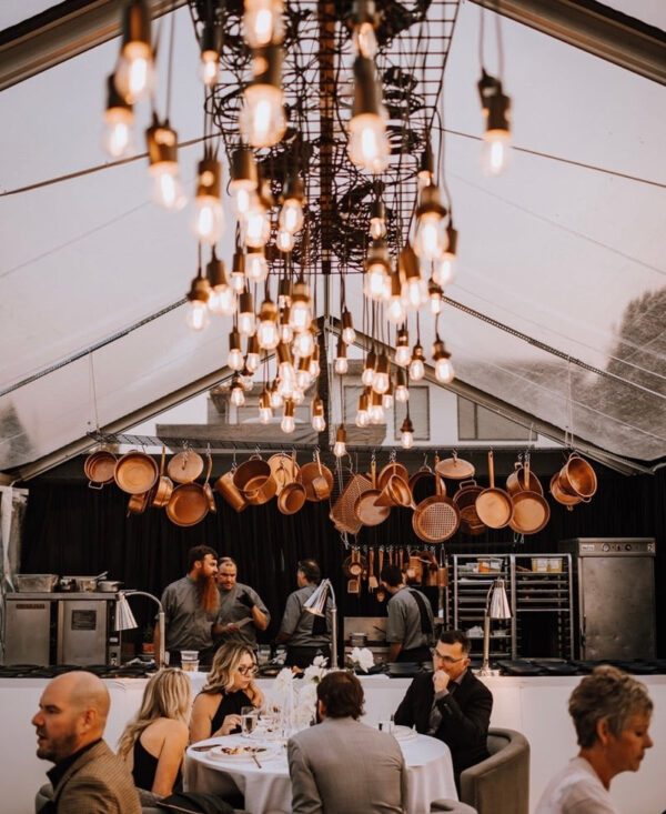 A group of people sitting at tables under an overhead light fixture.