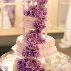 A three tiered cake with purple roses on top.