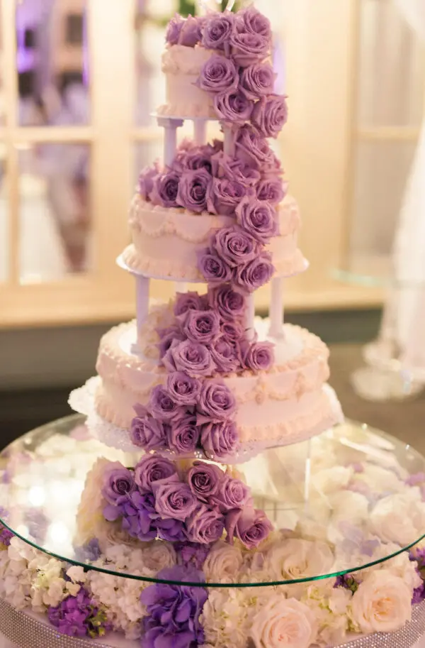 A three tiered cake with purple roses on top.