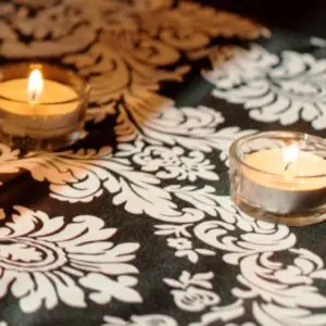 Two candles are lit on a table with a black and white floral print.