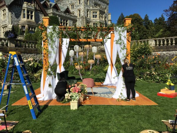 A couple of people standing in front of an outdoor wedding arch.