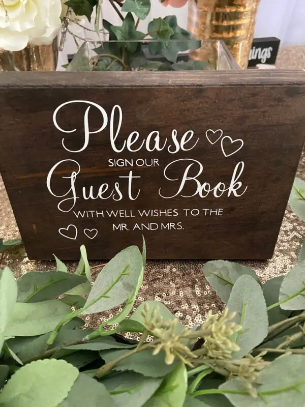 A wooden sign that says please sign our guest book with well wishes to mr. And mrs.