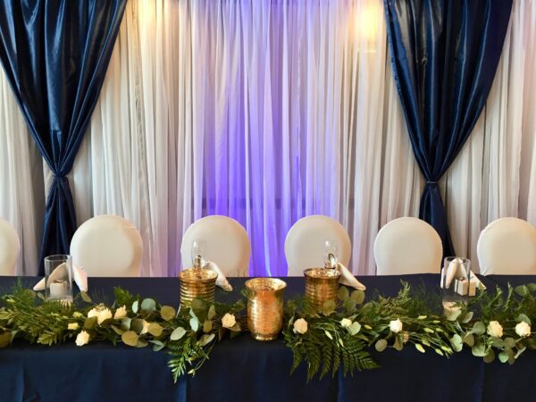 A table set up with white chairs and blue curtains.