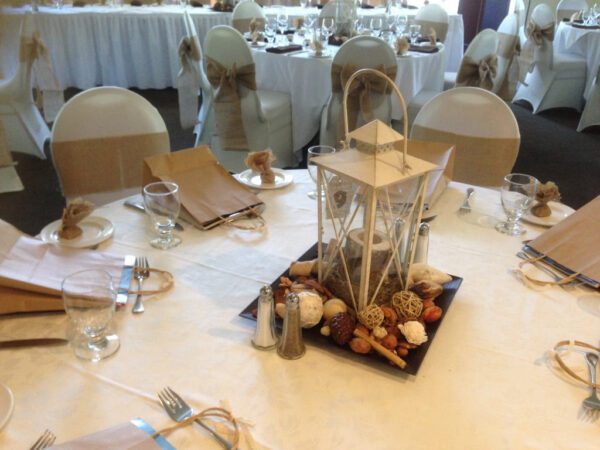 A table with white linens and a lantern on top of it.