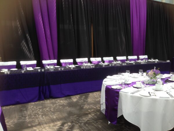 A table with purple and white linens in front of a black curtain.