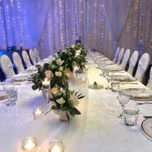 A long table with white chairs and flowers on it