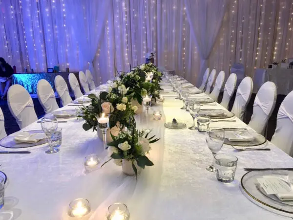 A long table with white chairs and flowers on it