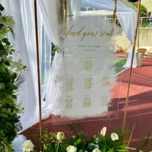 A wedding sign with flowers and greenery on the ground.