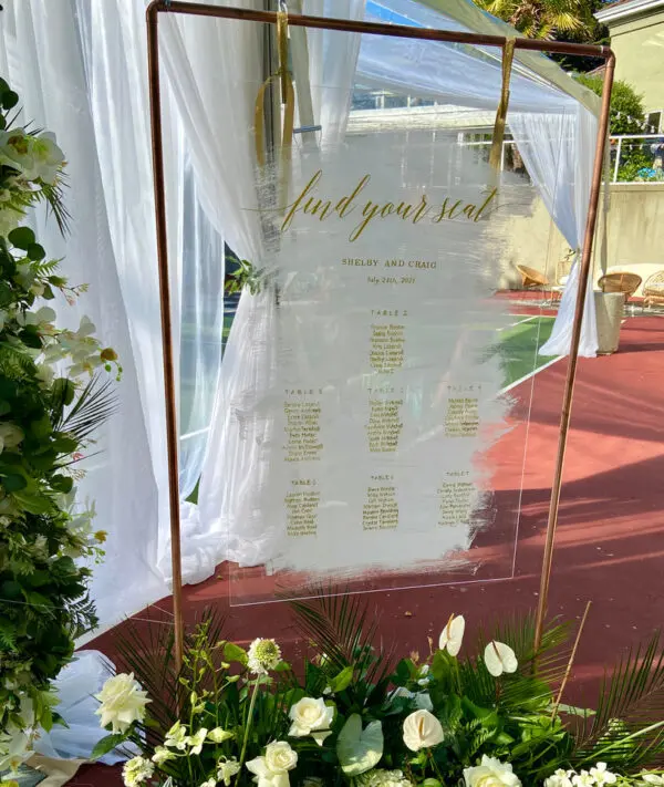 A wedding sign with flowers and greenery on the ground.