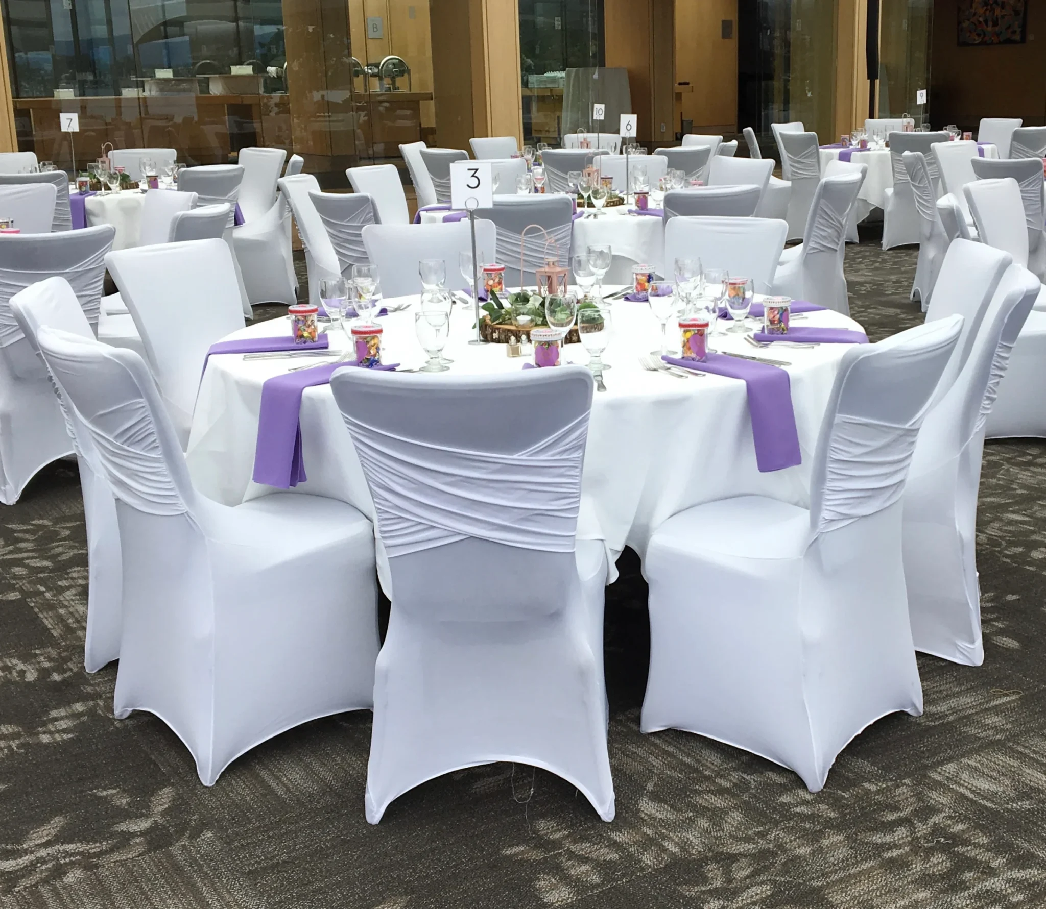 A table with white chairs and purple napkins.