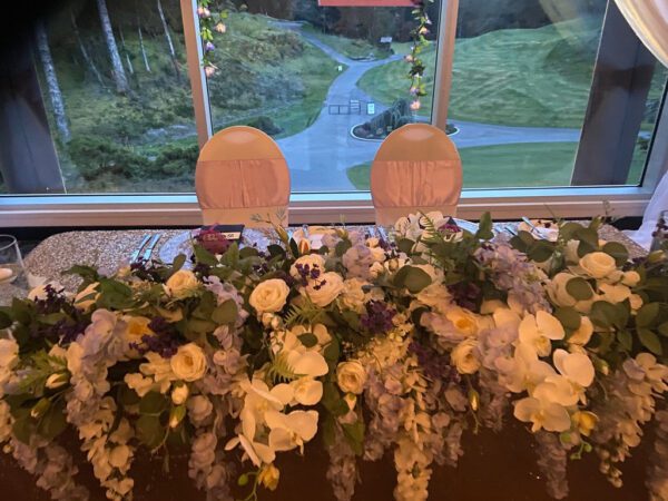 A table with flowers and chairs in front of a window.