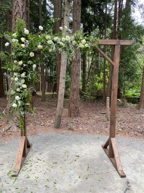 A wooden arch with flowers on it in the woods.