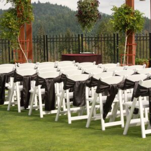 A row of white folding chairs with black sashes.