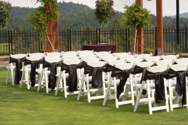 A row of white folding chairs with black sashes.