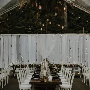 A long table with white chairs and lights hanging from the ceiling.