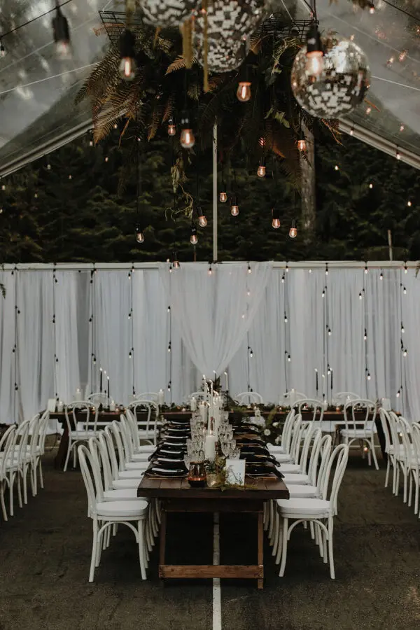 A long table with white chairs and lights hanging from the ceiling.