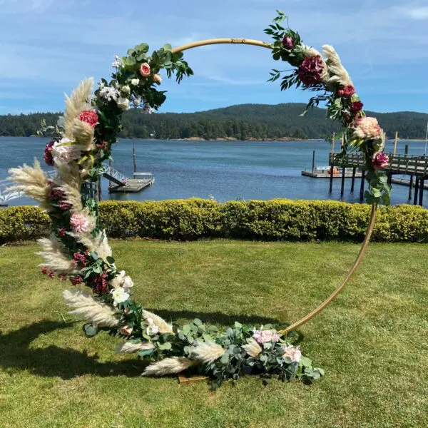 A circular arch with flowers and greenery in the grass.