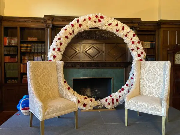 Two chairs in front of a fireplace with a wreath made out of roses.