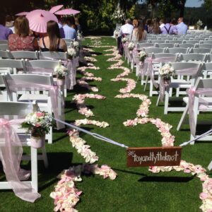 A wedding ceremony with pink flowers and white chairs.