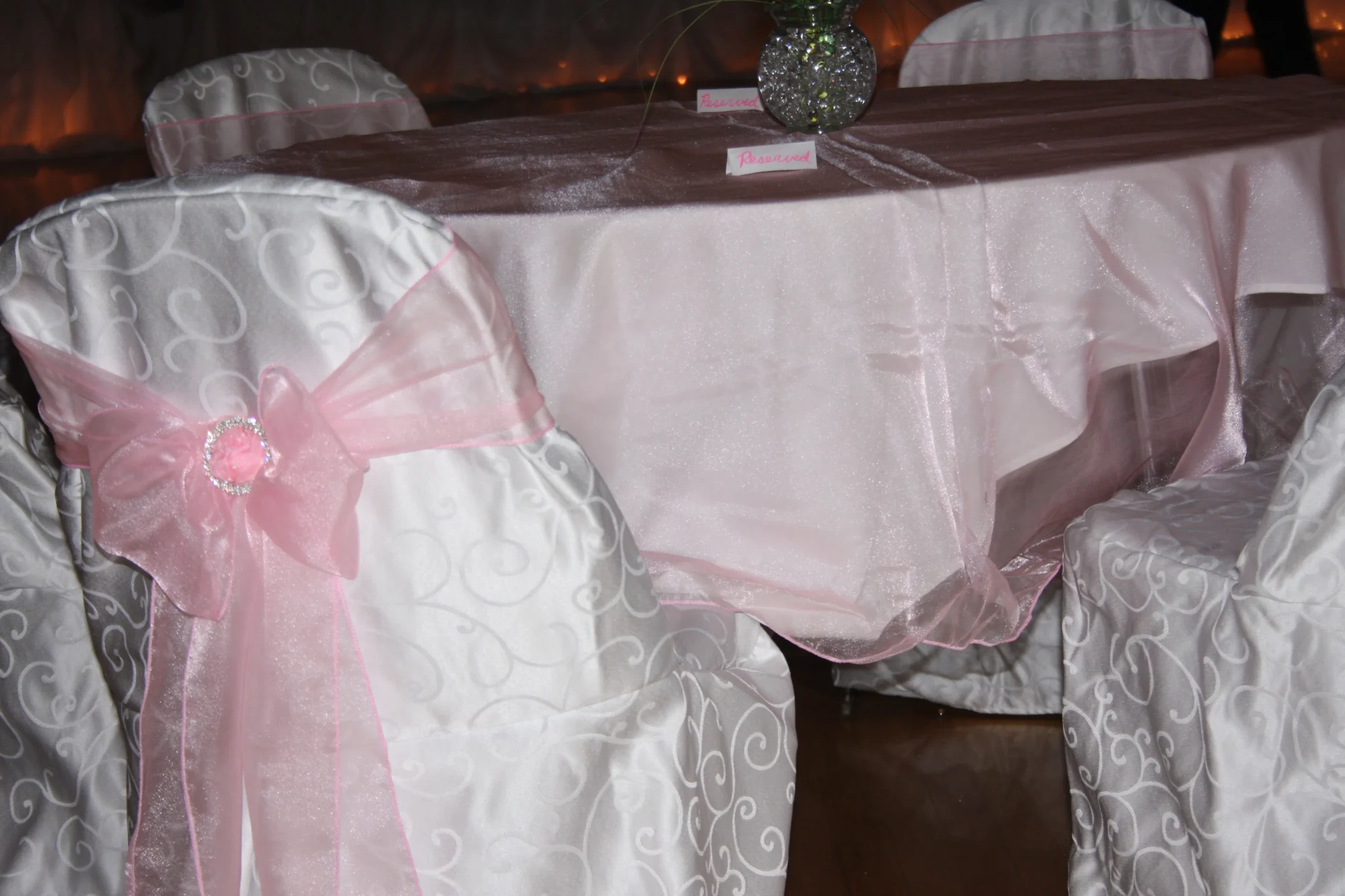 A table with pink and white chairs in front of a vase.