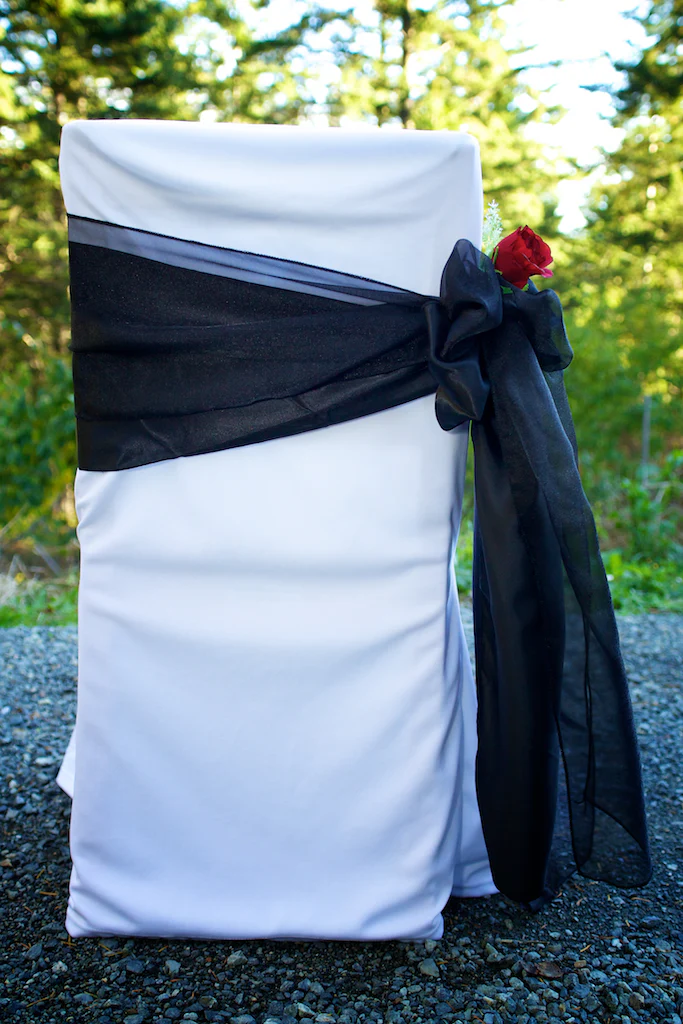 A white chair with black sash and red rose.