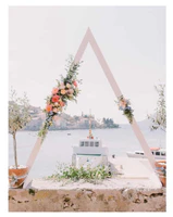 A triangle shaped wedding arch with flowers on top of it.