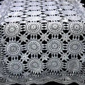 A table runner with white crochet flowers on it.