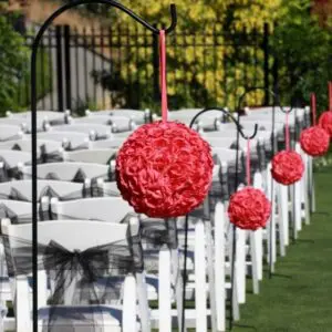 A row of white chairs with red flowers hanging from them.