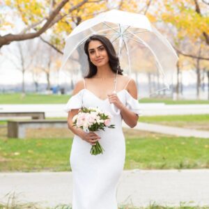 A woman in white holding an umbrella and flowers.