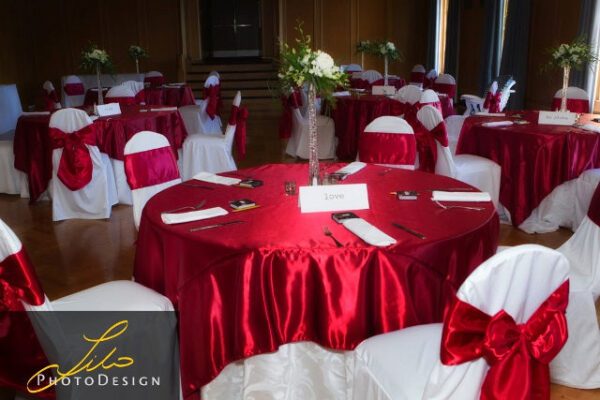 A room with many tables and chairs covered in red cloth.