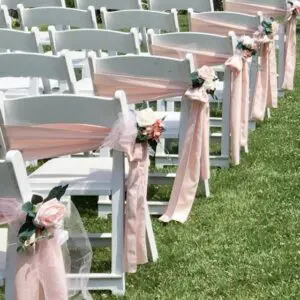 A row of white chairs with pink bows on them.