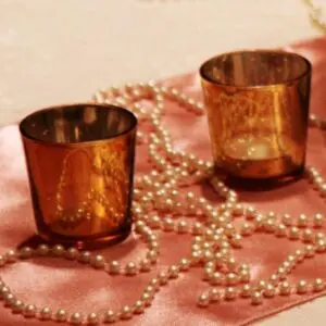 Two candles are sitting on a pink cloth with pearls.