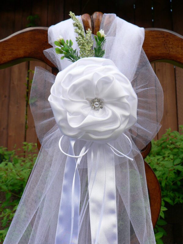 A white bow with flowers and tulle on the back of a chair.