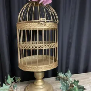 A gold bird cage with a pink flower in it.