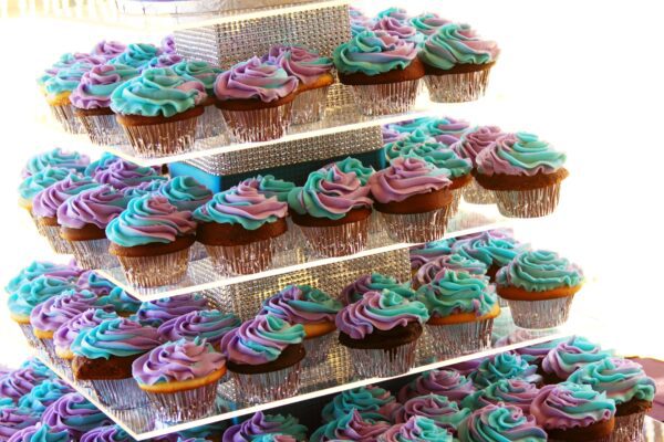 A display case filled with several cupcakes in different colors.