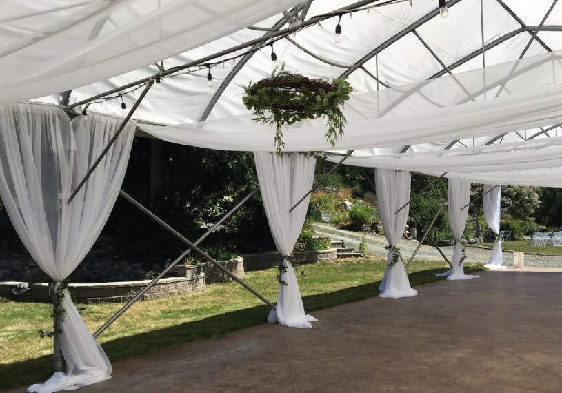 A tent with white curtains and greenery hanging from it.