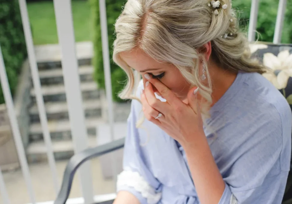 A woman sitting outside with her hand over her face.